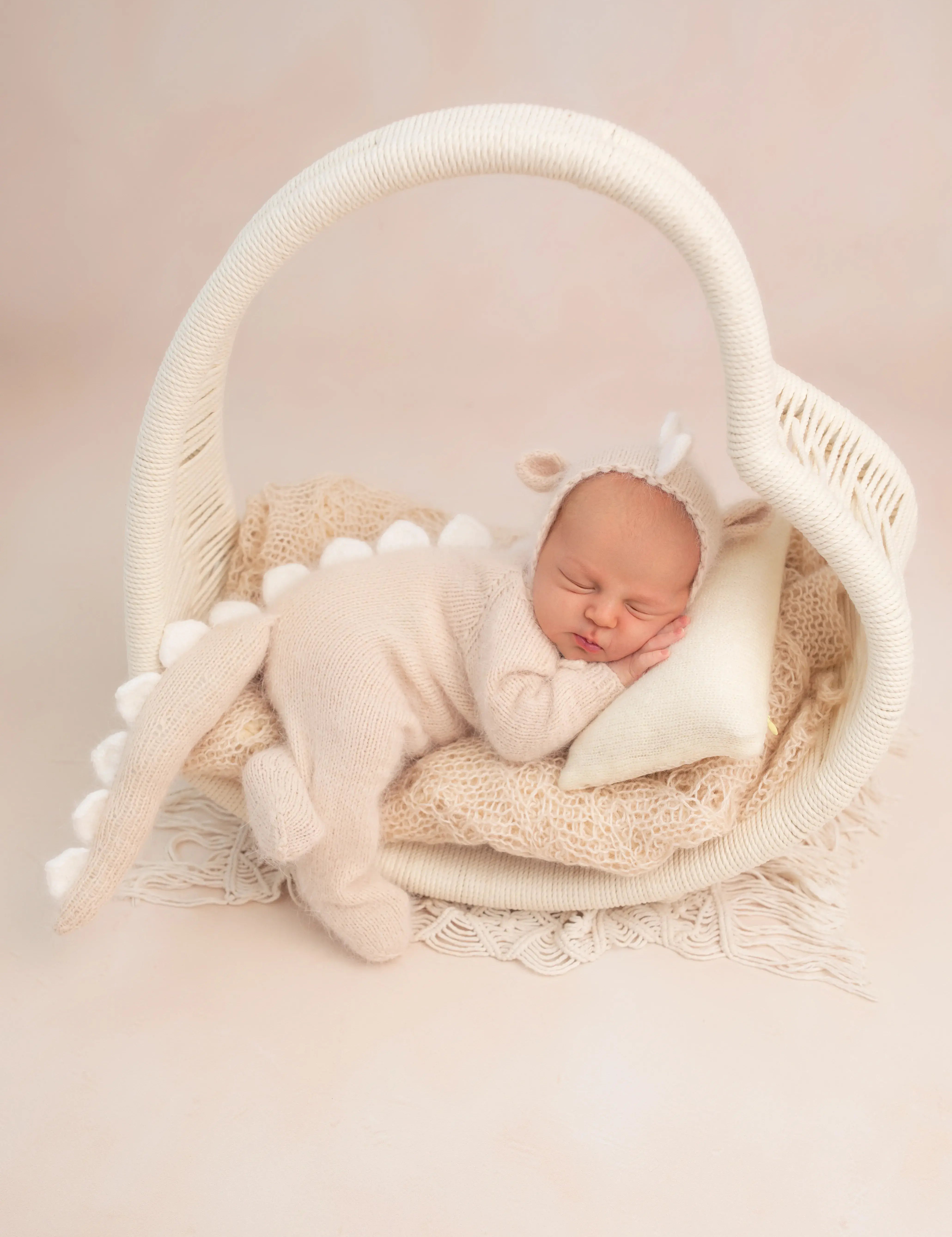 Newborn baby wrapped in a white blanket in a wicker basket on a beige background