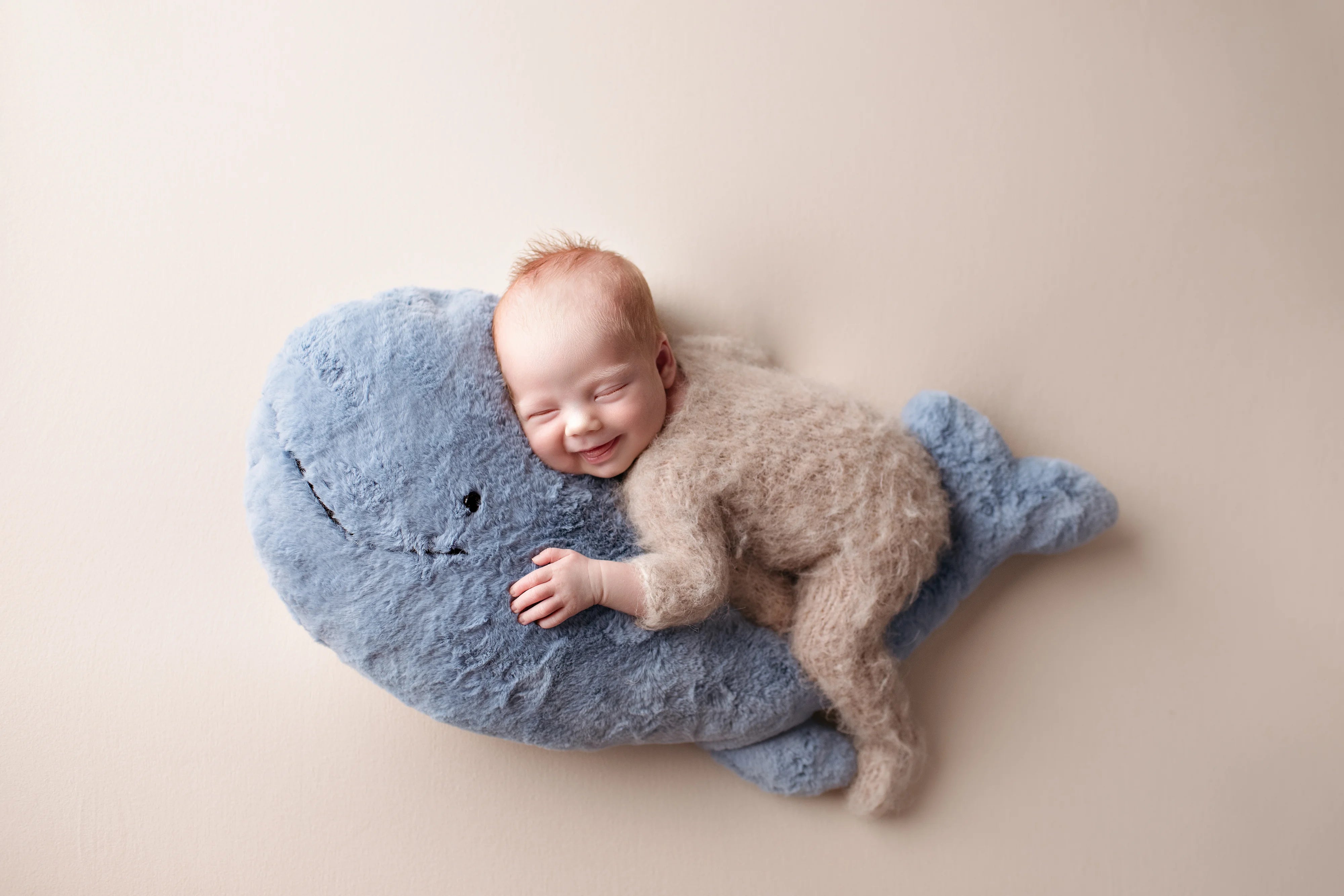 Newborn baby sleeping on a blue whale-shaped pillow against a beige background