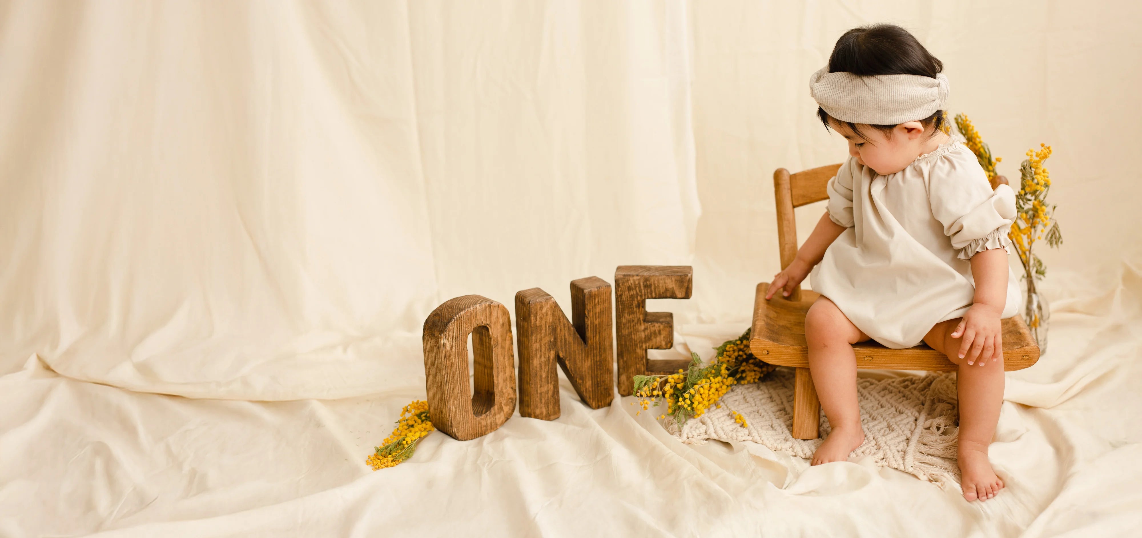 Child sitting on a chair next to wooden letters spelling 'ONE' on a white background