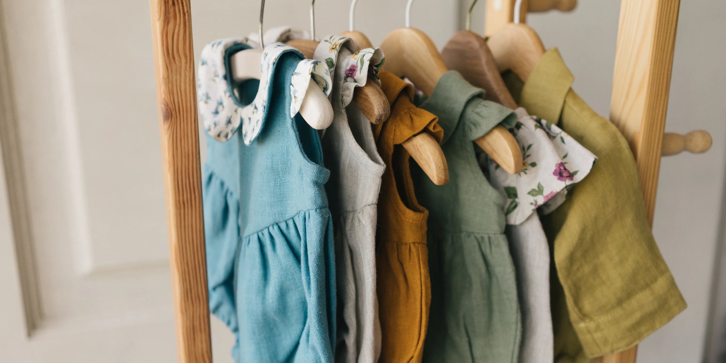 Children's clothing on hangers hanging on a wooden rack.