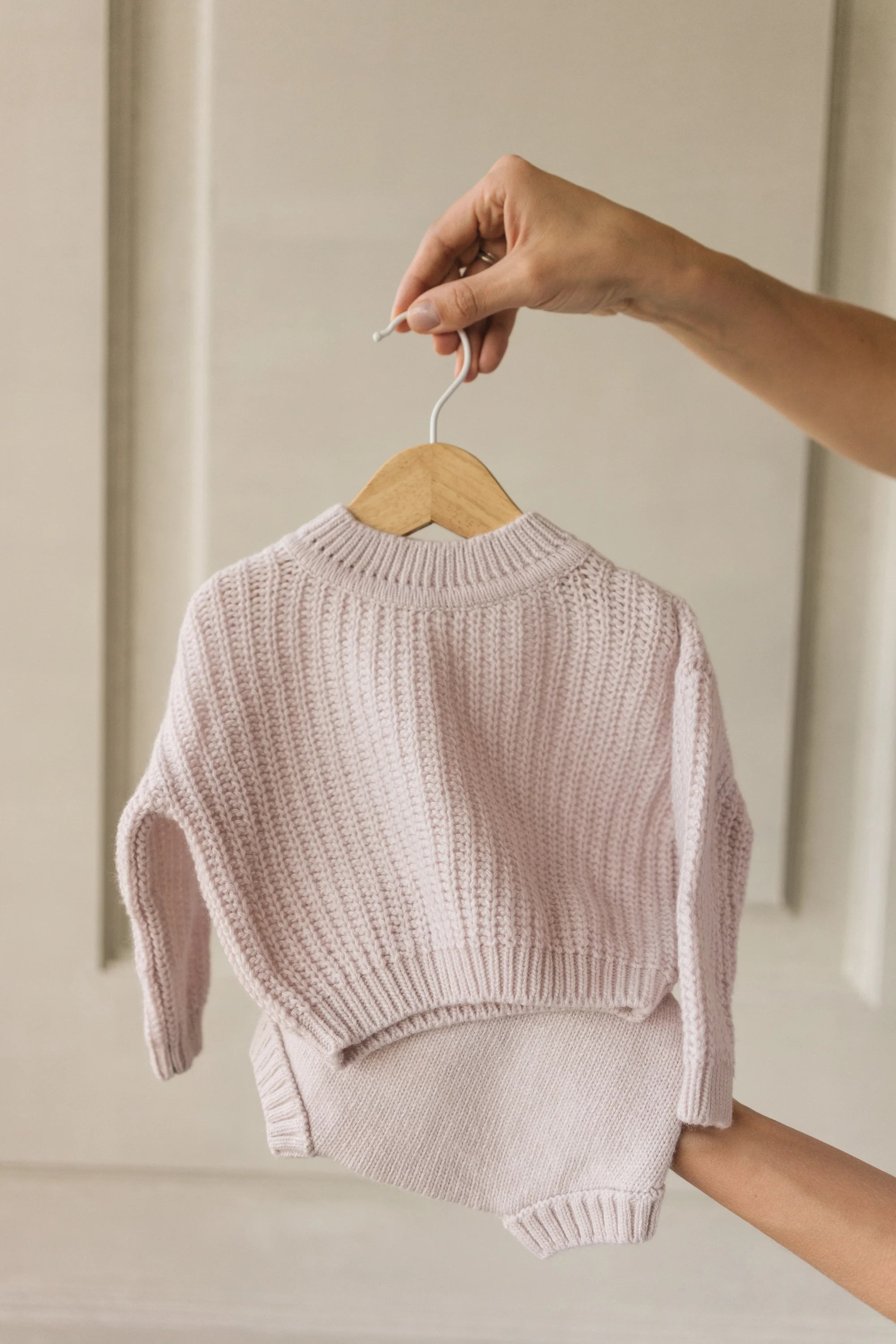 Baby sweater and pants set on a hanger against a neutral background