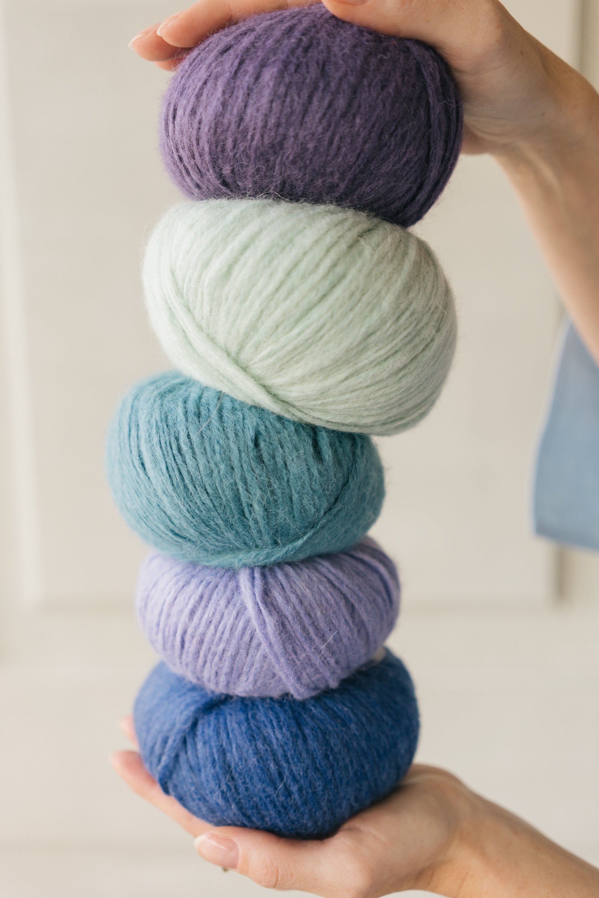 Stack of colorful yarn balls held in hands against a neutral background