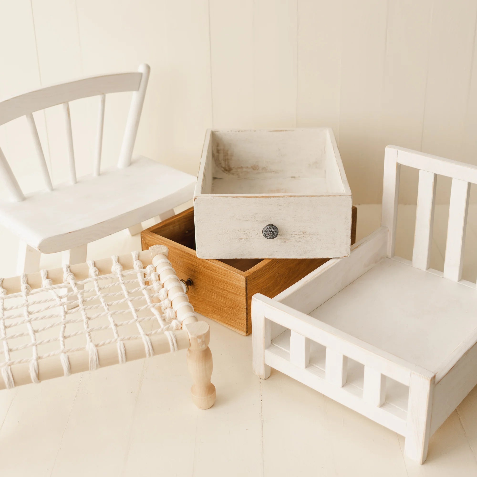 Wooden drawer with white top next to a small white bed and chair on a light wooden floor.