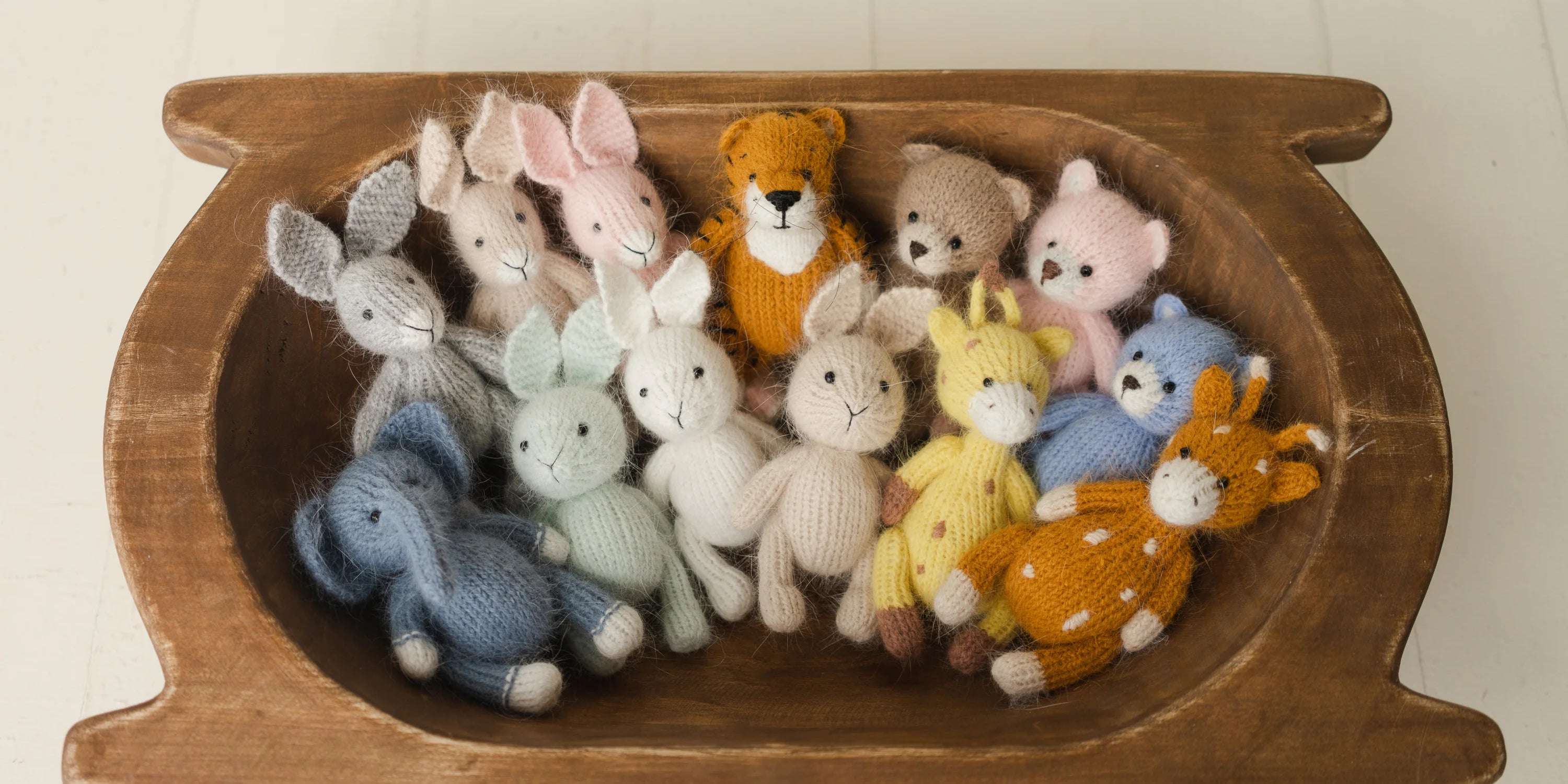 Wooden basket with knitted toy animals on a light background