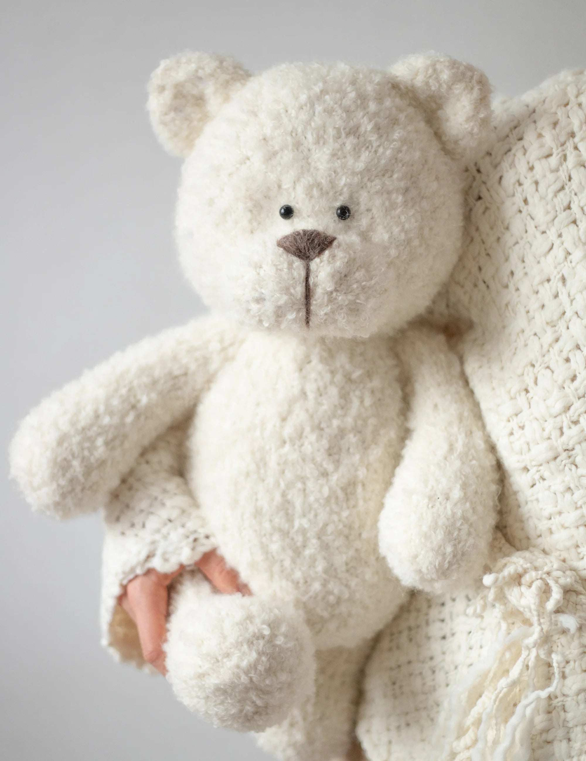 White teddy bear held by a person wearing a white sweater against a light gray background