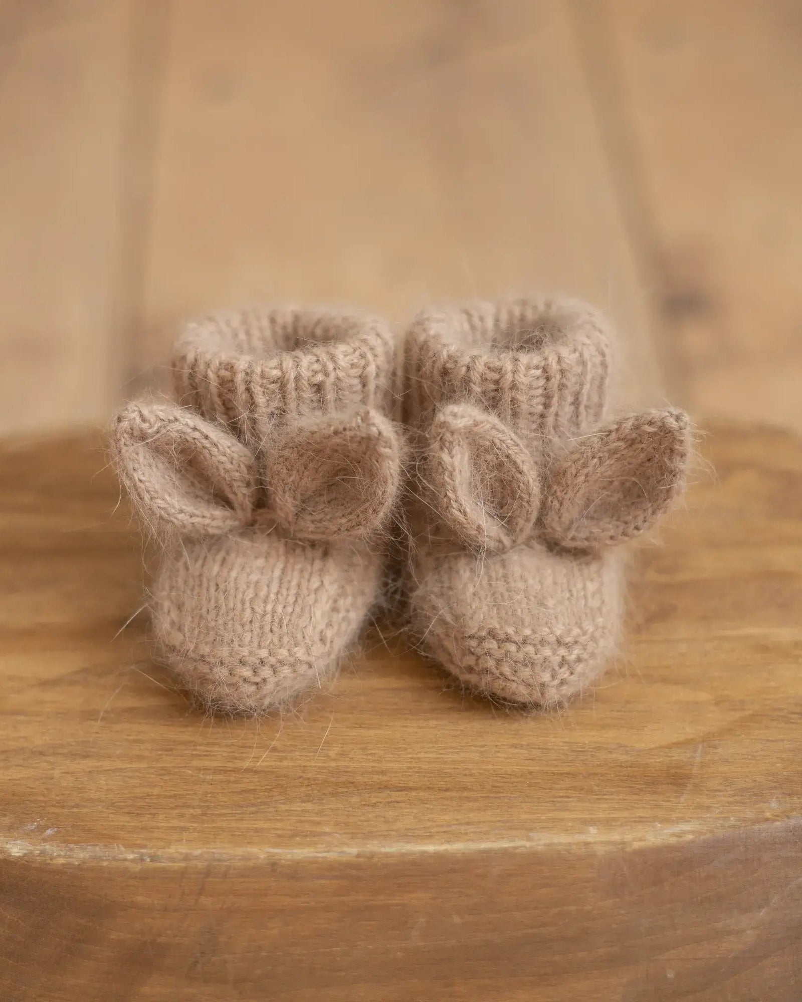 Pair of knitted baby booties with bunny ears on a wooden surface