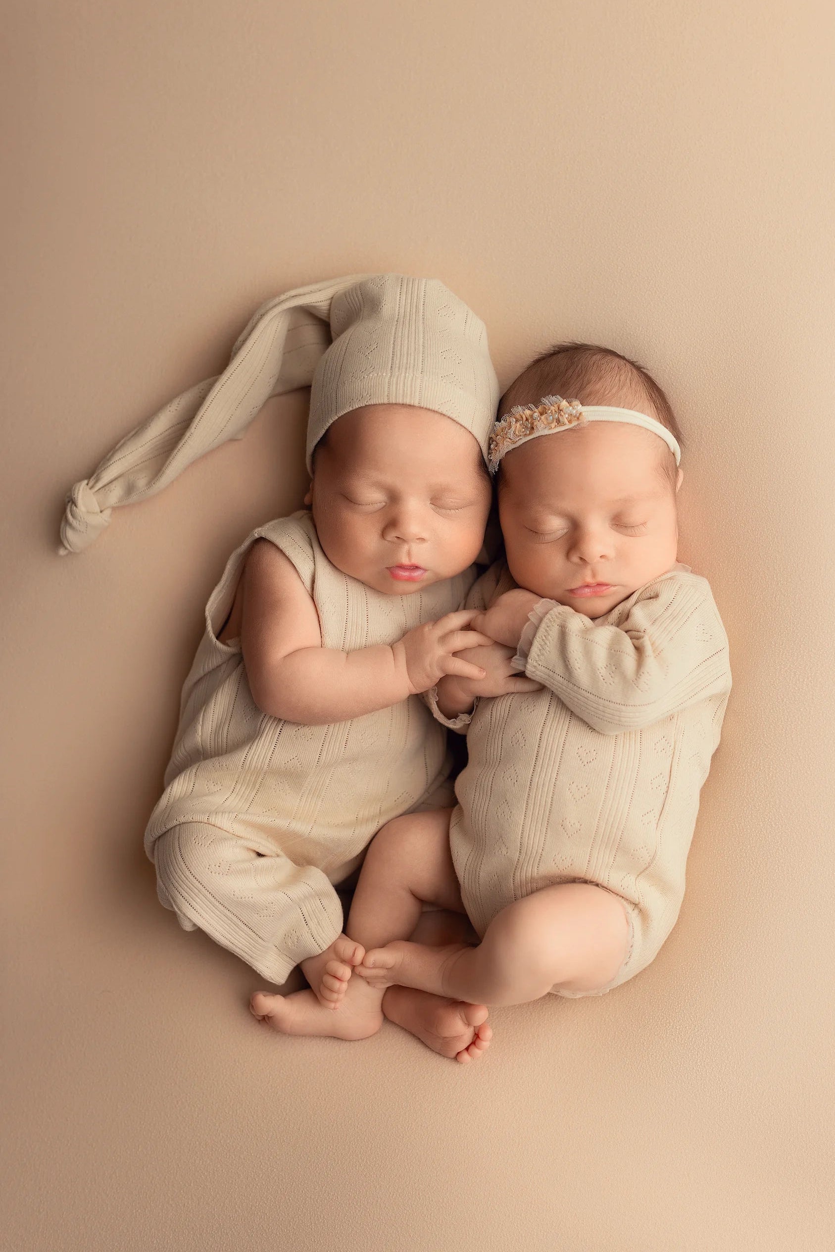 Two newborn babies in matching outfits and headbands lying on a beige surface.