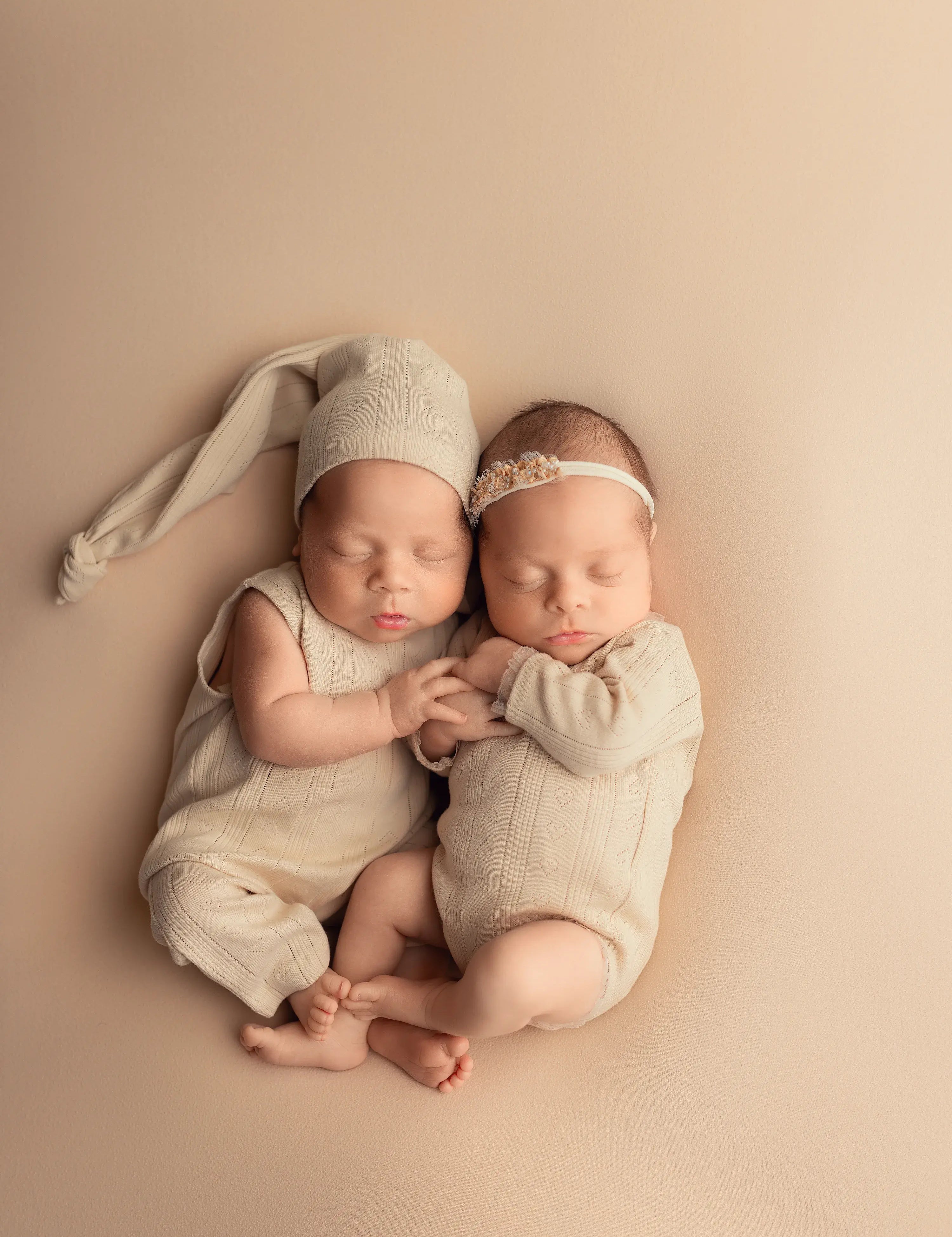 Two newborn babies in matching outfits lying on a beige surface.