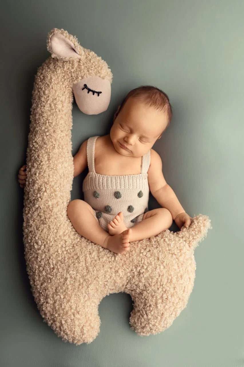 Baby sitting on a large plush llama toy against a plain background