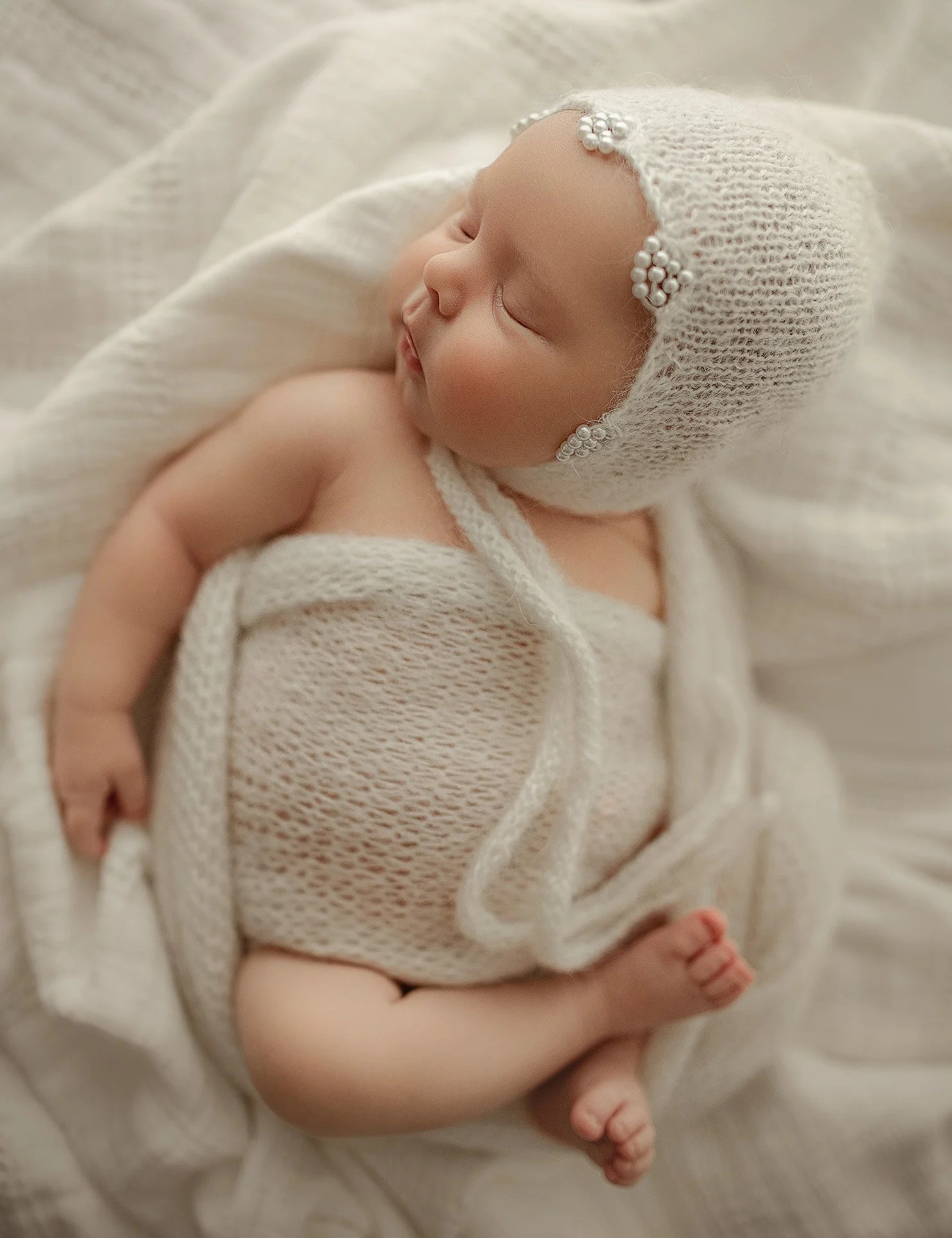 Newborn baby wrapped in a knitted outfit and bonnet on a soft white background
